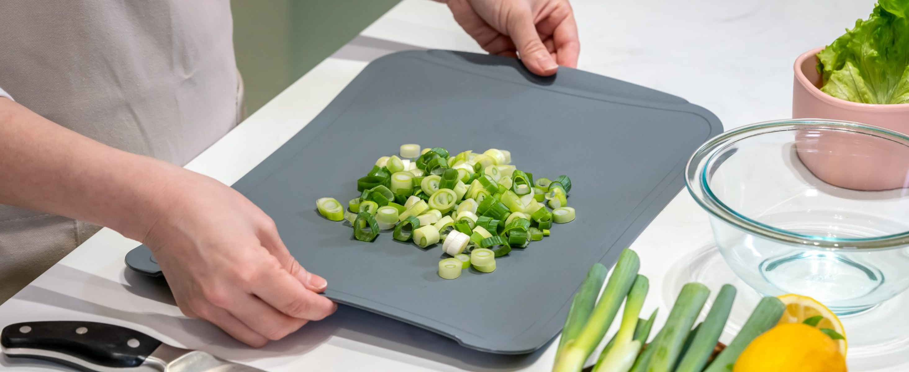 A person uses the built in handles on a flexible cutting board to lift the board off of a countertop