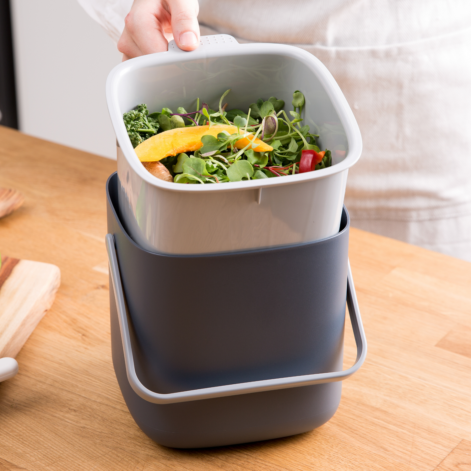Compost bin with fresh kitchen waste on a wooden surface
