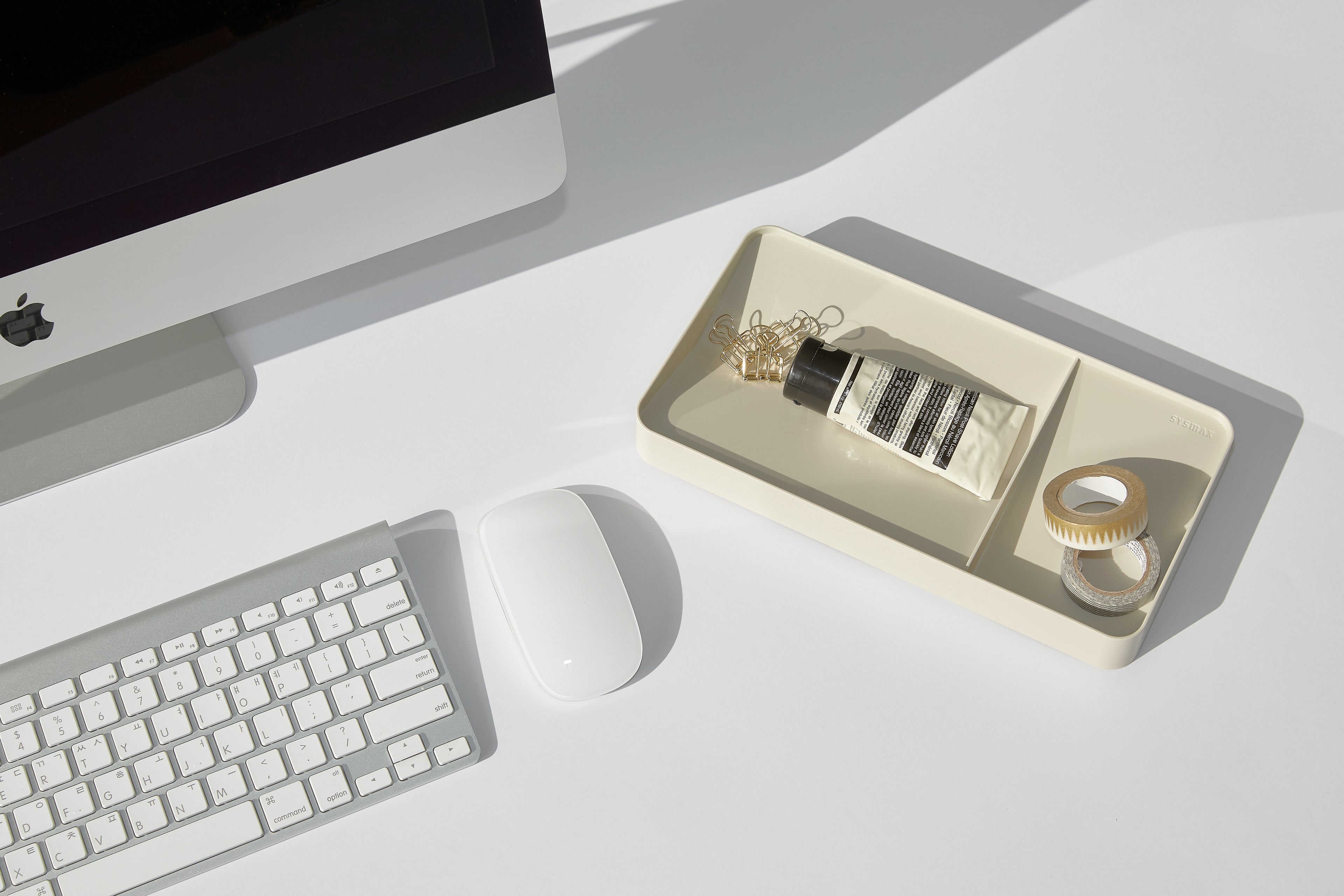 Computer setup with keyboard, mouse, and decorative items in a beige tray on a white surface