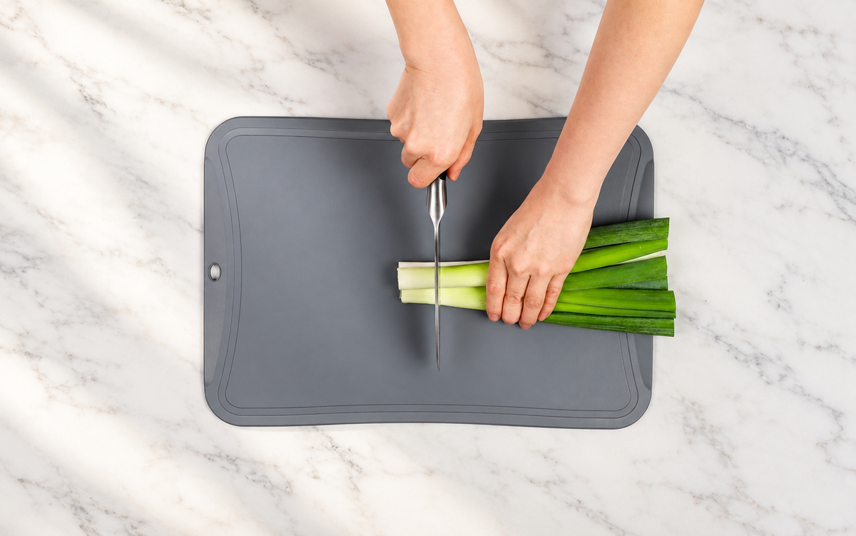 Slicing green onions on a gray Blue Ginkgo cutting board on marble.