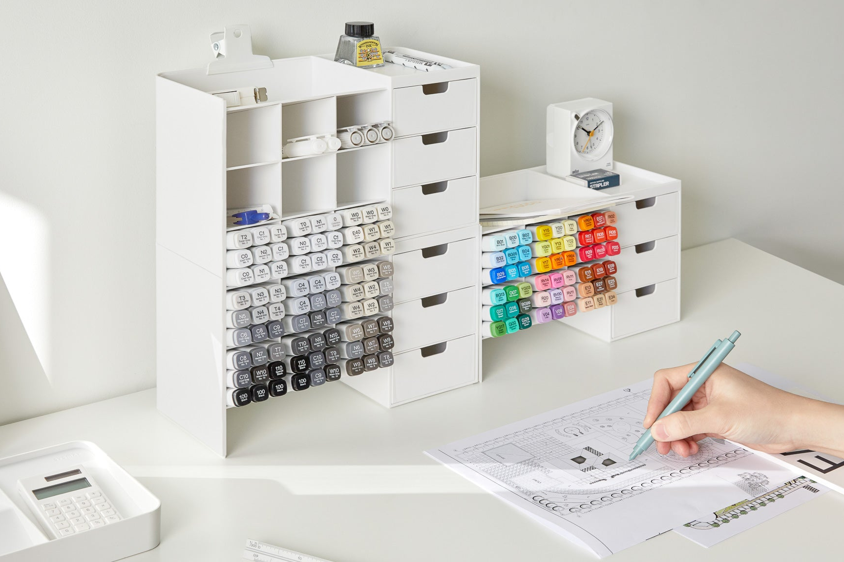 White stackable desk organizer with colorful markers and a person working on a document.