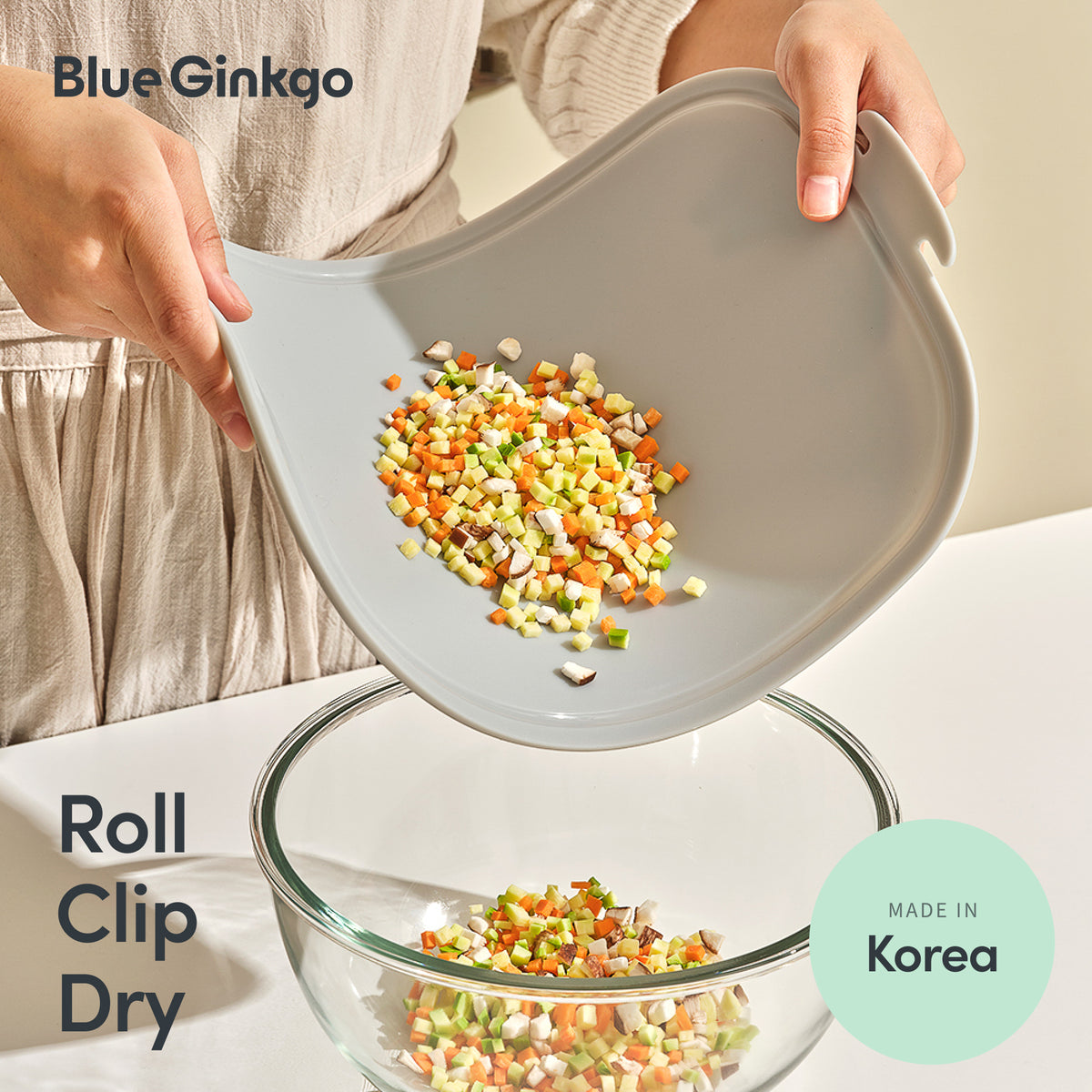 Hands bending a grey Blue Ginkgo silicone cutting board to funnel chopped vegetables into a bowl.
