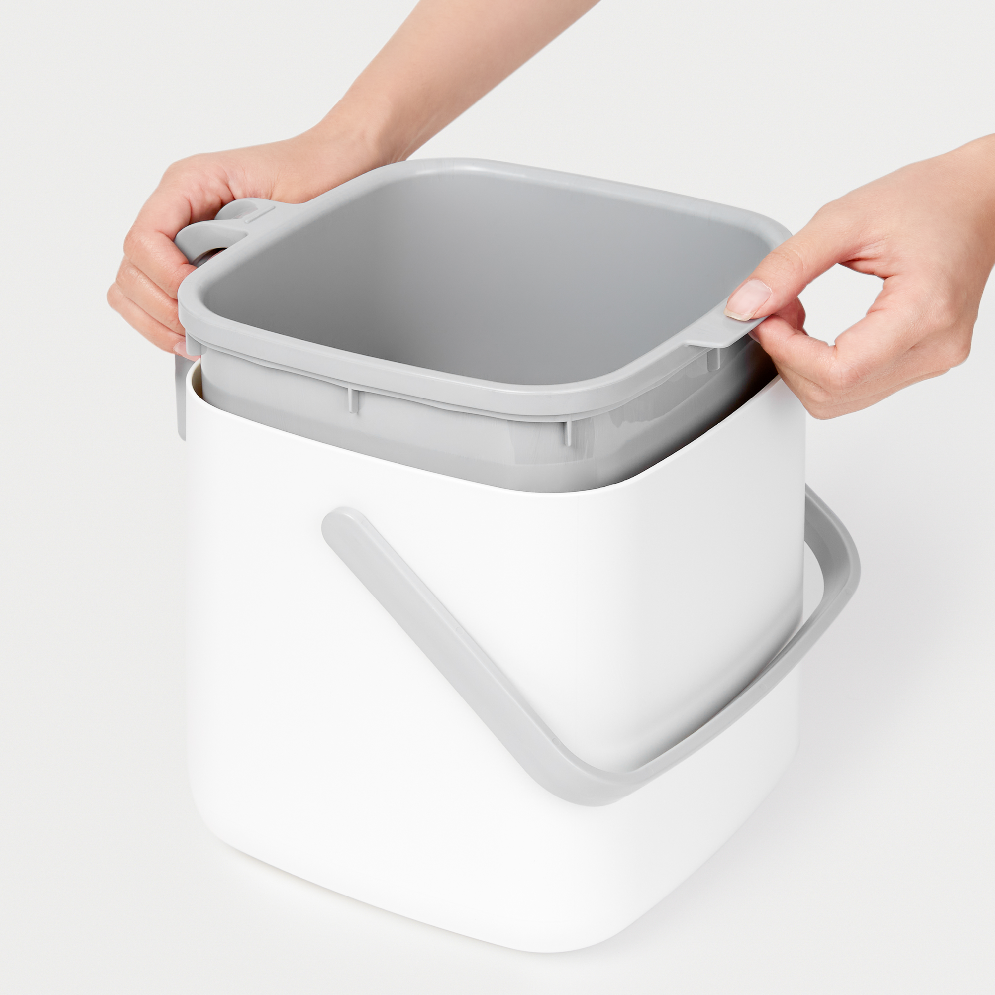 Person removing the gray food waste bin basket from a white compost bin