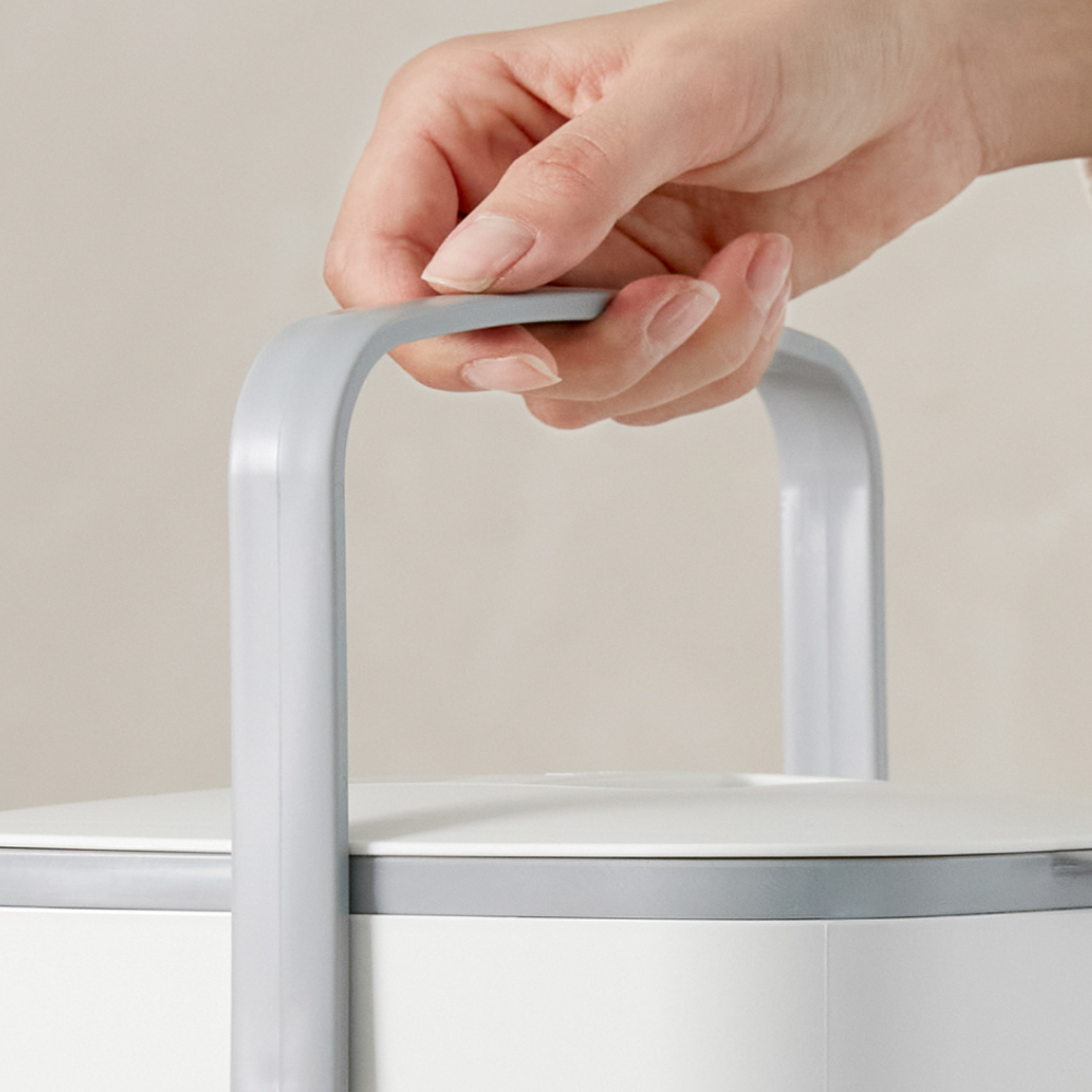 Hand holding a white compost bin by its grey handle