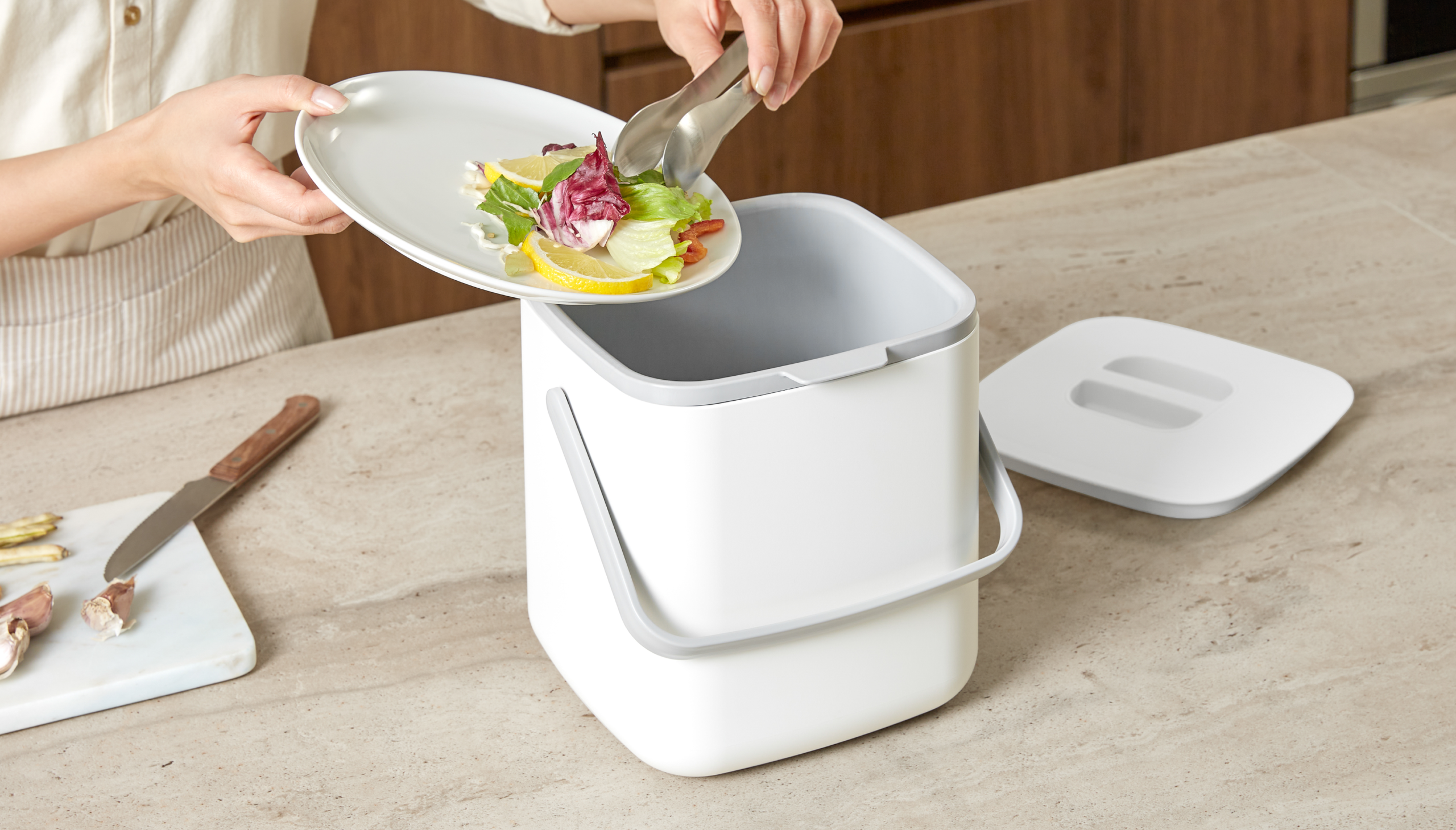 Person placing food waste into a kitchen compost bin.