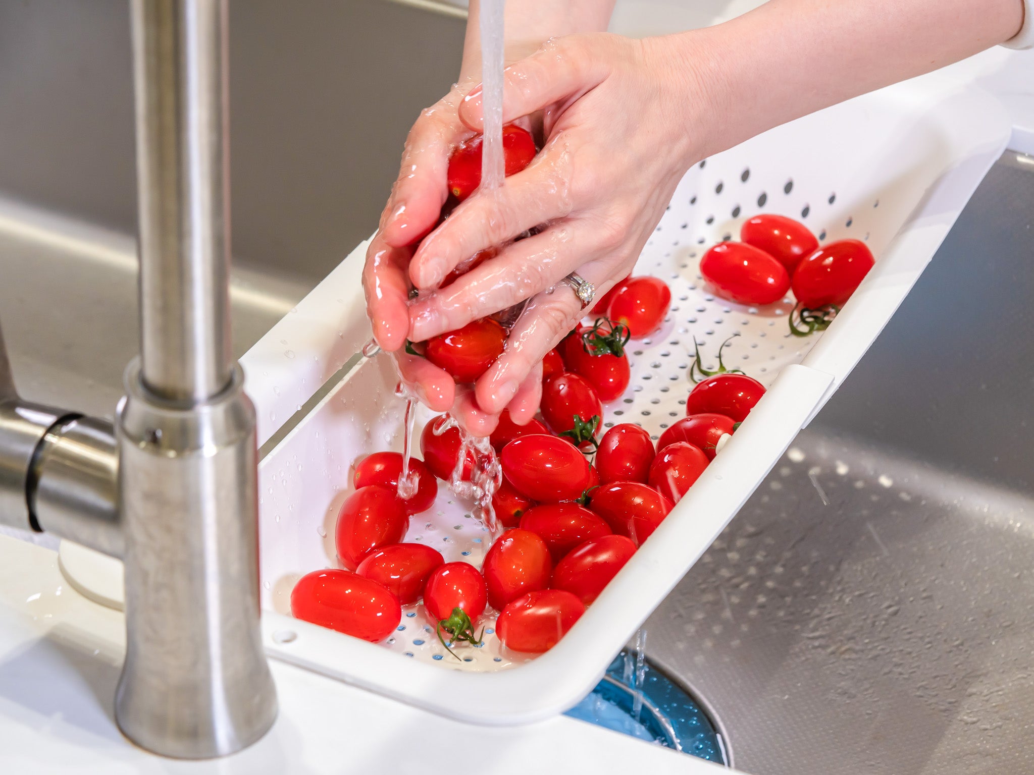 White over-the-sink colander being used to rinse small red tomatoes